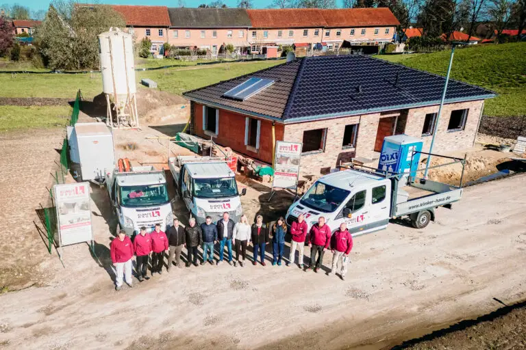 Team von KLINKER HAUS vor einem Rohbau mit Firmenfahrzeugen